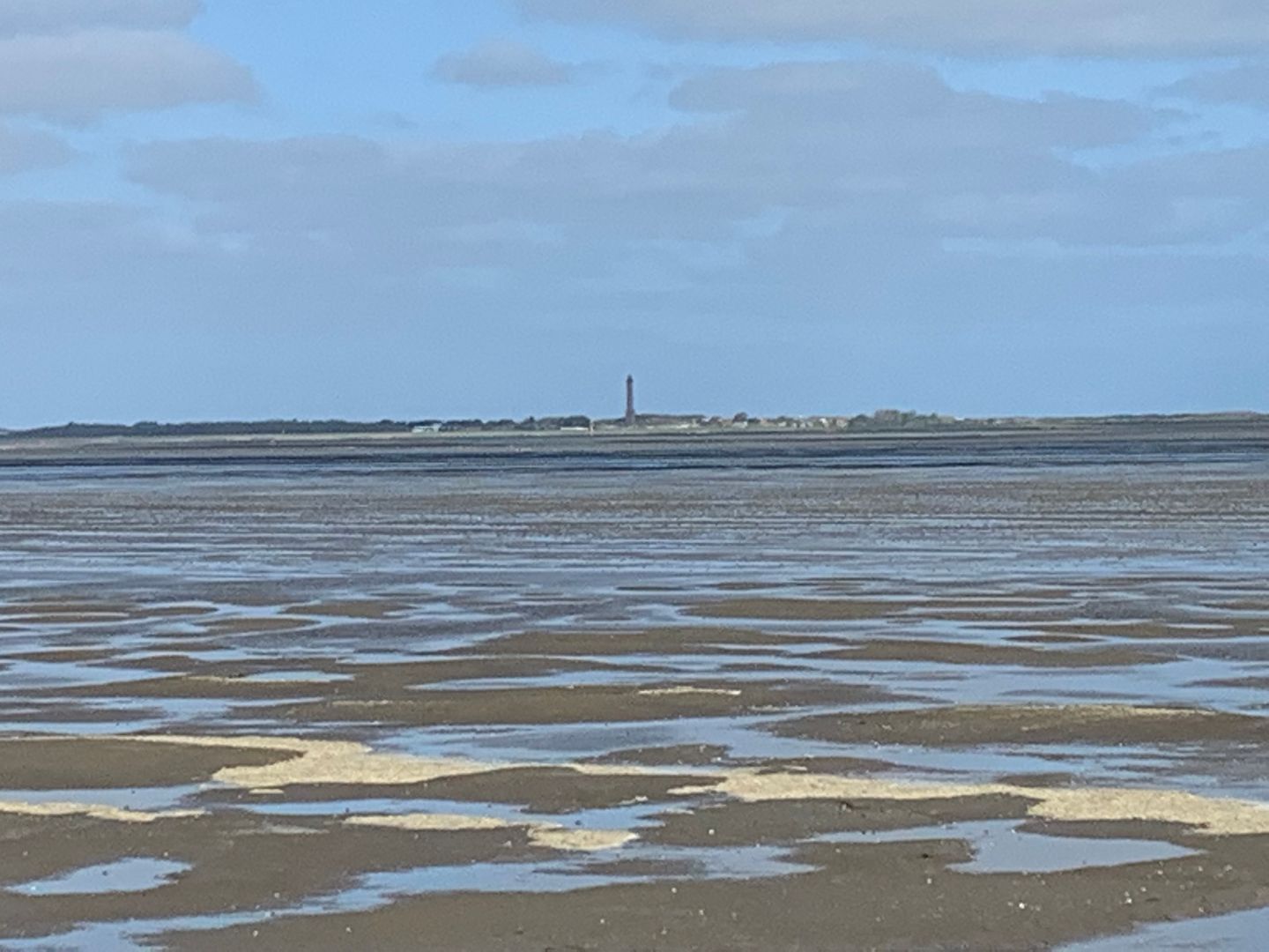 A wide, open beach with wet sand and a distant lighthouse.