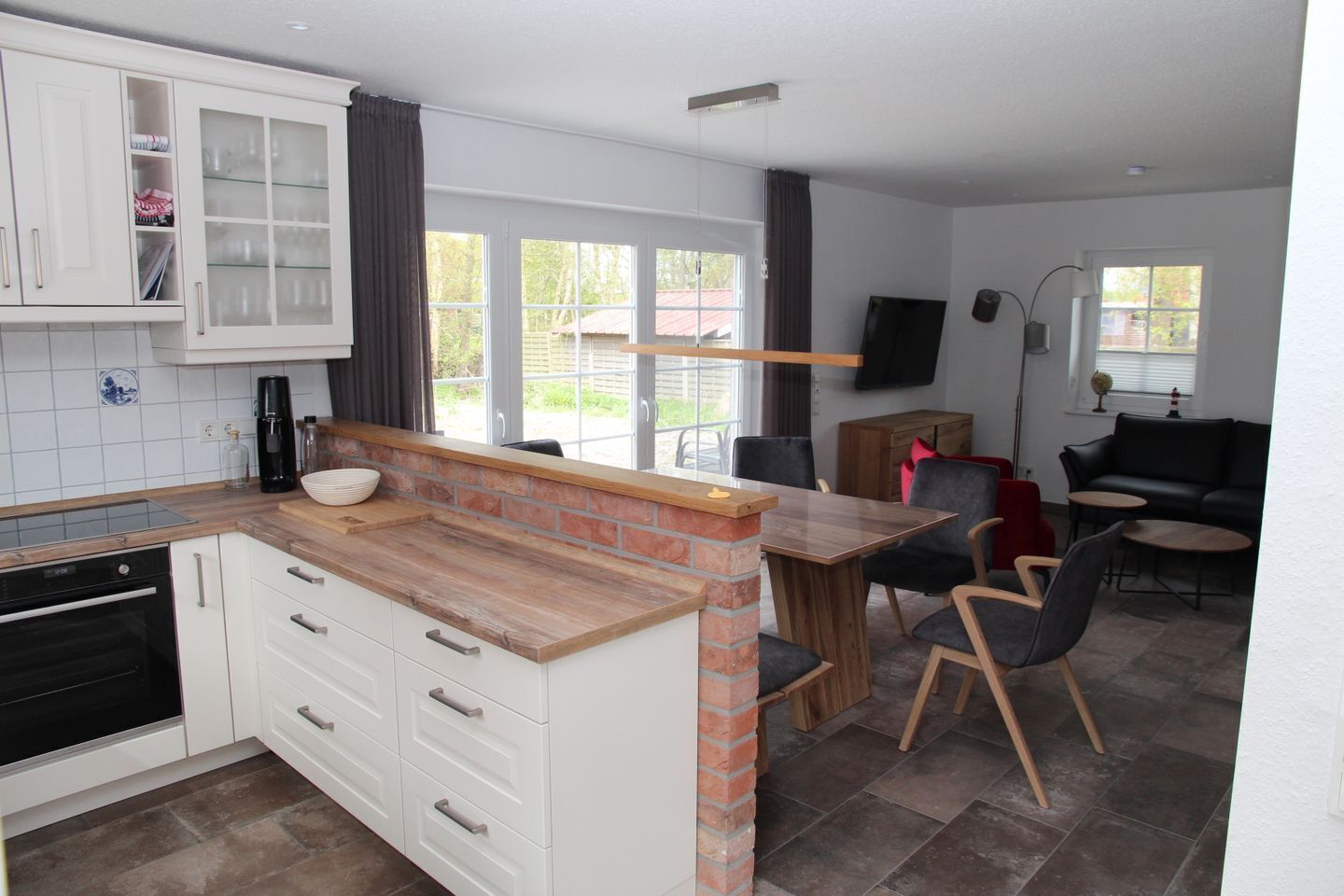 Una cocina moderna con armarios blancos, una pared de ladrillo decorativa y un comedor con mesa y sillas de madera.
