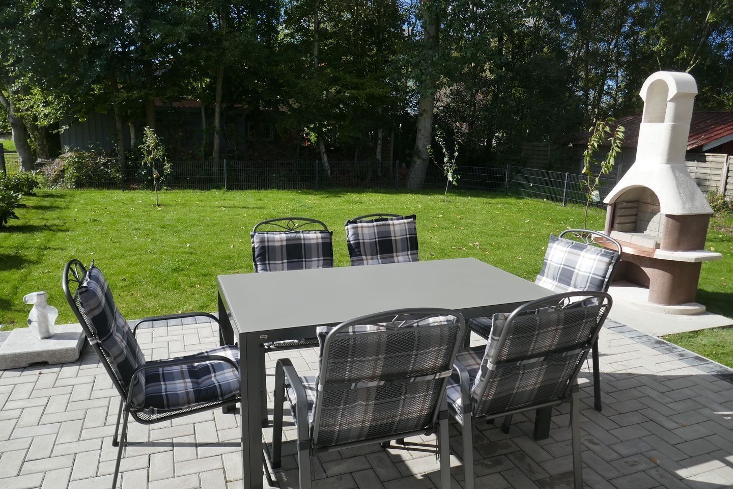 Eine Terrasse im Freien mit Tisch und vier Stühlen, einer kleinen dekorativen Skulptur und einem Steinofen.