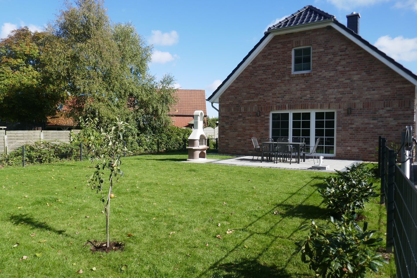 A brick house with a patio, a small tree, and a fence.