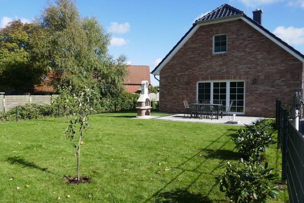 Une maison en briques avec un patio, un petit arbre et une clôture.