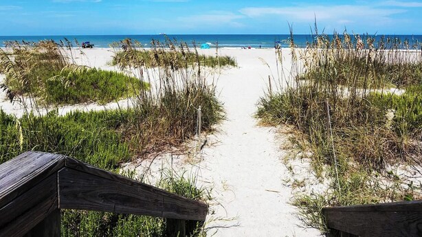 A sandy beach path leading to the ocean with a wooden structure on the left.