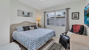 A bedroom with a bed, a chair, a desk, a ceiling fan, and a window with blinds.