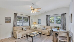 A living room with a sofa set, a coffee table, a dining table with chairs, a ceiling fan, and a window with curtains.