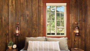 A wooden room with a bed, two nightstands, a window, and two wall-mounted lanterns.