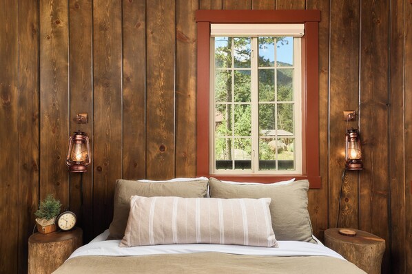 Una habitación de madera con una cama, dos mesitas de noche, un ventanal y dos faroles fijados a la pared.