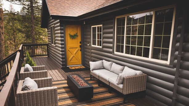 Une cabane en rondins dotée d’une véranda, de meubles en osier et d’un foyer.