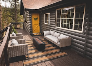 Una cabaña de troncos con porche, muebles de mimbre y una chimenea exterior.