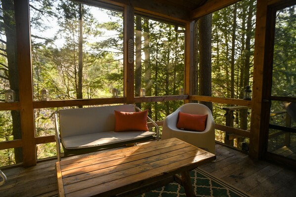 Terraza de madera con un banco y sillas, con vistas a un bosque.