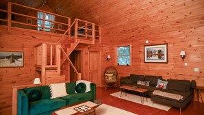 Ein gemütliches Blockhaus-Interieur mit einem grünen Sofa, einem braunen Sofa, einer Holztreppe und einer Holzdiele.