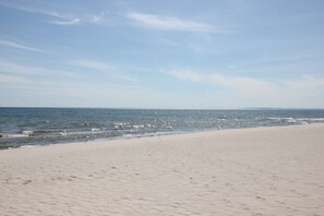 A wide sandy beach with gentle waves and a clear sky. - Die Ferienwohnung Dünenrose im Haus Südperd - Haus Südperd (Mönchgut)