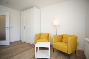 Ein Zimmer mit einem weißen Kleiderschrank, zwei gelben Sesseln, einem weißen Beistelltisch und einer Stehlampe.