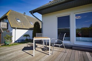 A wooden deck with a table and chairs, a large window, and a house with a tiled roof.