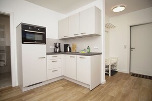 A compact kitchen with white cabinets, a built-in oven, a coffee maker, and a small countertop. - Die Ferienwohnung Dünenrose im Haus Südperd - Haus Südperd (Mönchgut)