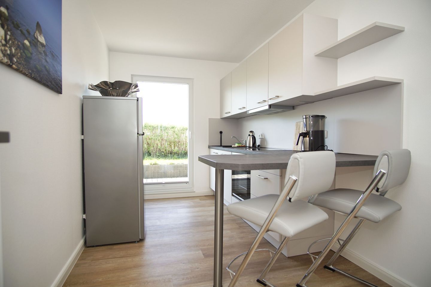 A compact kitchen with a refrigerator, a coffee maker, and a chair.