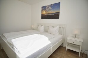 Quarto branco com cama, duas mesas de cabeceira e uma luminária na parede.
