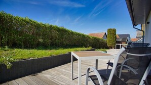An outdoor deck with a table and chairs, surrounded by a hedge and a view of a house. - Haus Südperd Ferienwohnung Strandwinde - Haus Südperd (Mönchgut)