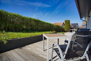 Una terraza al aire libre con una mesa y sillas, rodeada de un seto y vistas a una casa.
