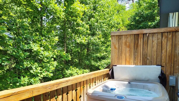 Un bain à remous sur une terrasse en bois, avec une clôture en bois et une végétation luxuriante en arrière-plan.