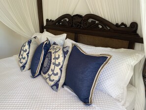 A bed with a white quilted cover and four decorative pillows in shades of blue and beige.