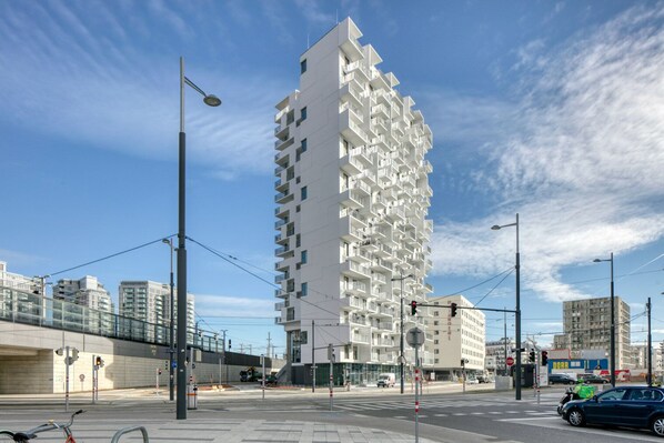 A modern high-rise building with balconies, located at a city intersection with traffic lights and a pedestrian crossing.