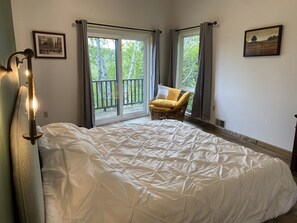 Relax in this serene bedroom with a large bed, wicker chair, and framed artwork.