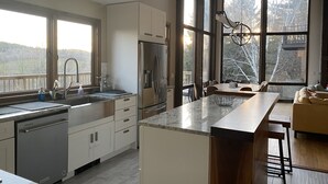 Une cuisine moderne dotée d’un grand îlot central, d’appareils électroménagers en acier inoxydable et offrant une vue sur l’extérieur grâce à de grandes fenêtres.