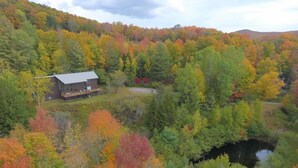 Une cabane entourée d’un feuillage automnal et bordée d’un petit étang.