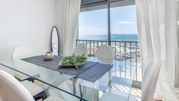 Ein moderner Balkon mit einem Glastisch, Stühlen und Blick aufs Meer.