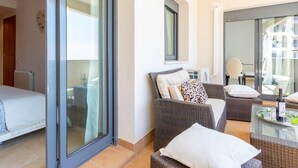 Ein moderner Balkon mit Rattanmöbeln, einer Glastür und Blick auf die Stadt.