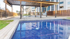 Ein Schwimmbecken mit einer hölzernen Pergola darüber, umgeben von einer Holzterrasse und einem Zaun.