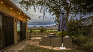 Un patio con mobiliario exterior, luces de cadena y vistas a montañas.