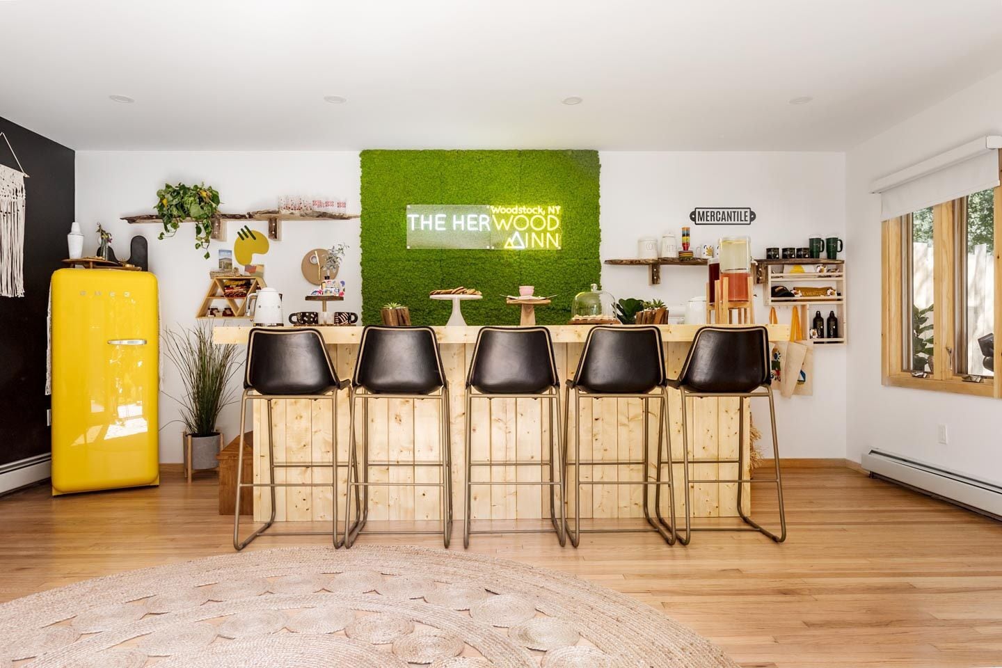 Een moderne keuken met een groene wand, houten barstoelen, een gele koelkast en diverse keukenbenodigdheden.