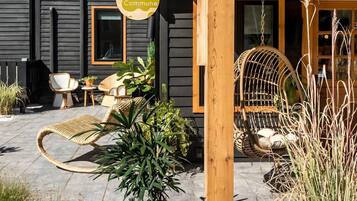 Un bâtiment moderne à l’extérieur sombre, avec une véranda en bois meublée de meubles en osier et une enseigne suspendue sur laquelle on peut lire « The Commune ».