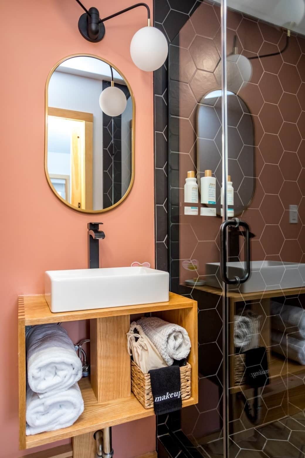 A bathroom with a round mirror, a white sink, and a wooden shelf with towels.