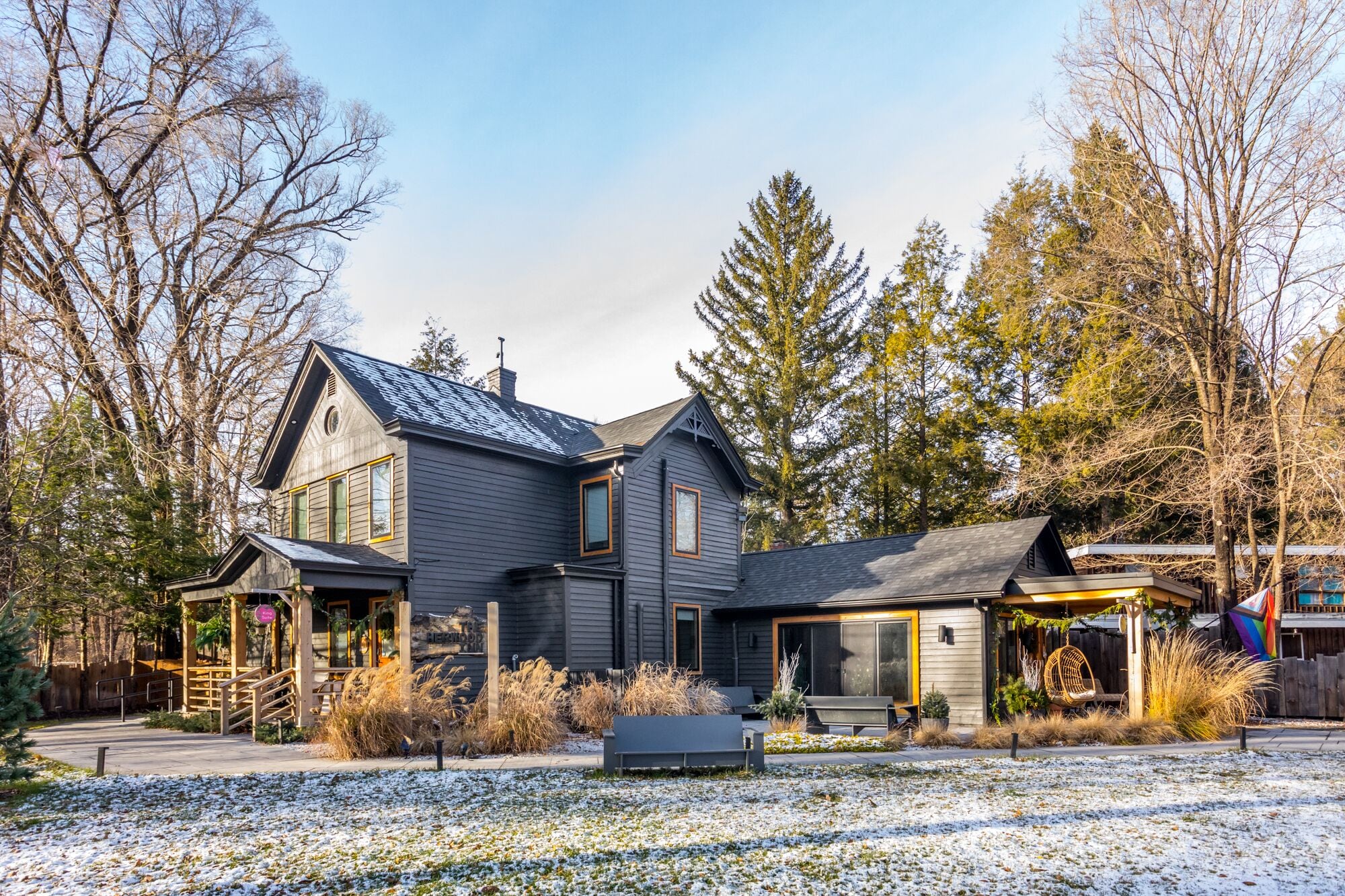 A two-story house with a dark gray exterior, a sloped roof, and a front porch with a swing chair.