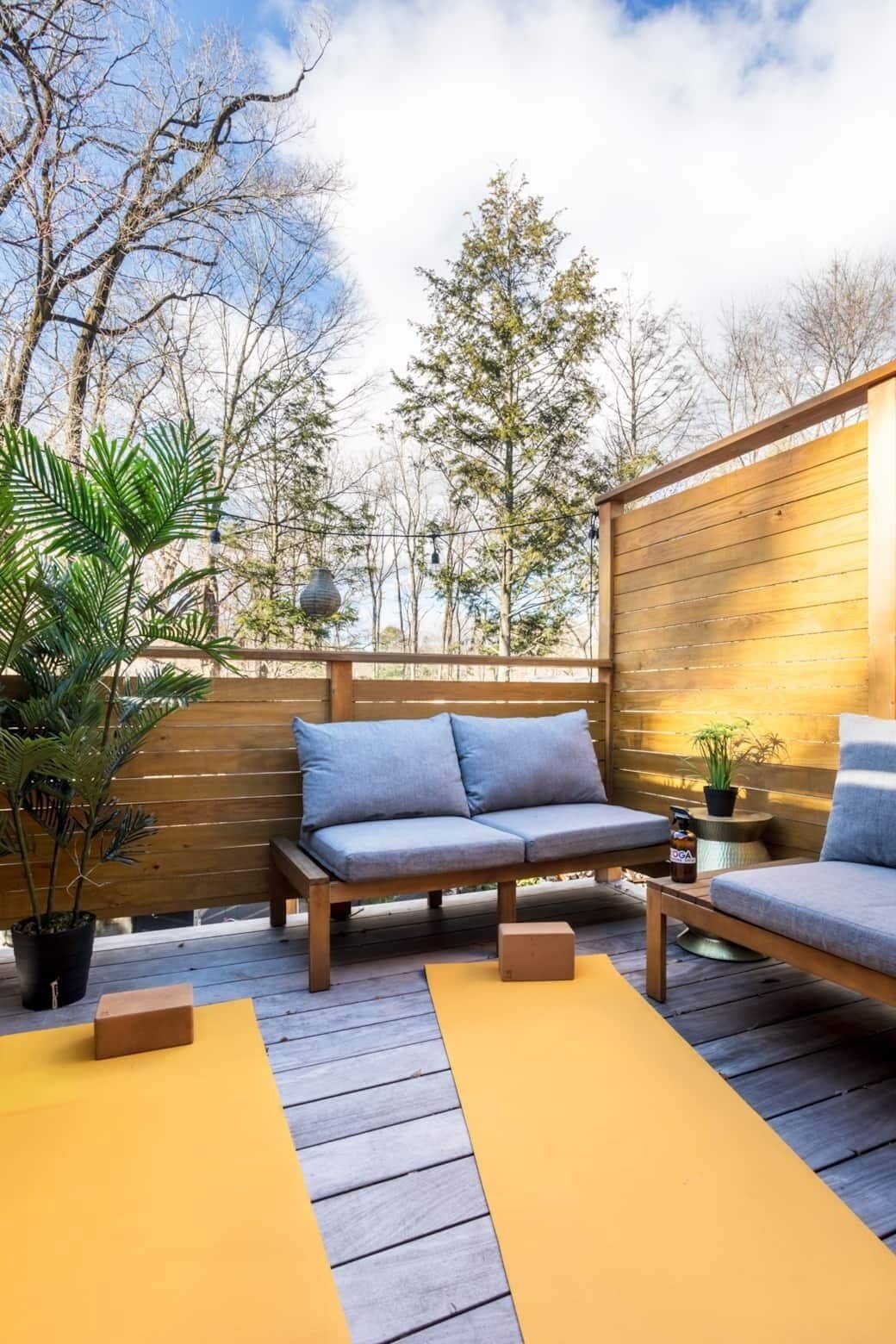 Un patio al aire libre con terraza de madera, dos sofás grises, una mesita y una planta en maceta.