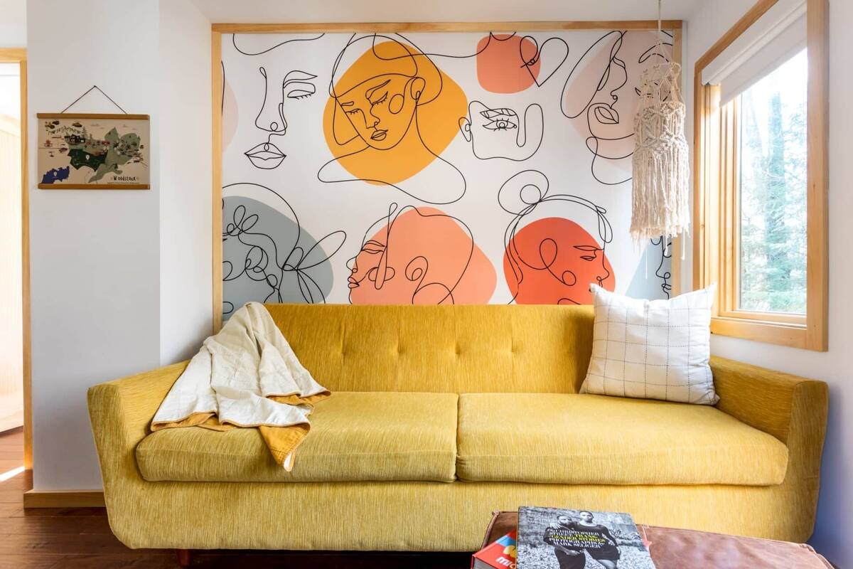 A yellow sofa with a white throw blanket and a cushion, positioned in front of a wall with abstract line art and a map.