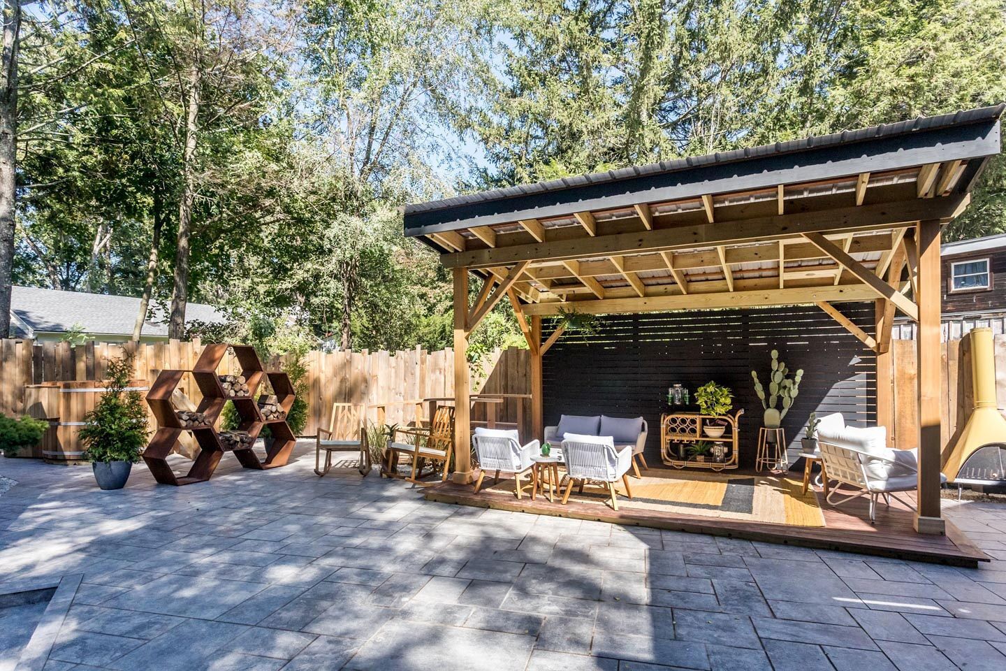 A covered outdoor patio with wooden furniture, a fire pit, and a hexagonal planter.