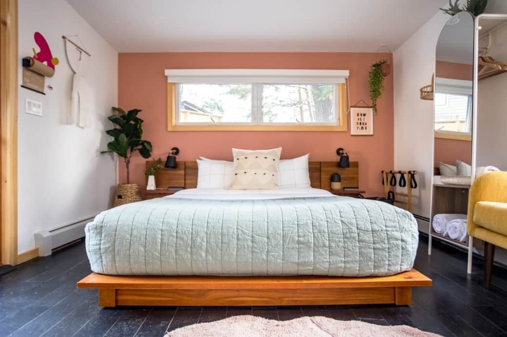 A bedroom with a bed, bedside tables, a mirror, a plant, and a window.