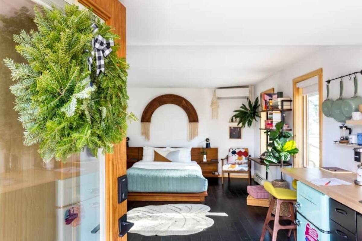 A modern bedroom with a bed, a small desk, and a kitchenette area.