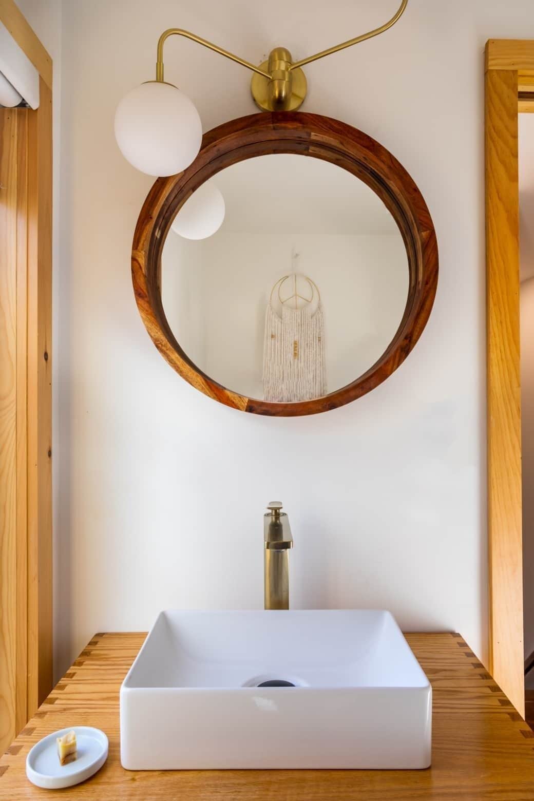 A bathroom with a wooden vanity, a white sink, and a round mirror with a wooden frame.