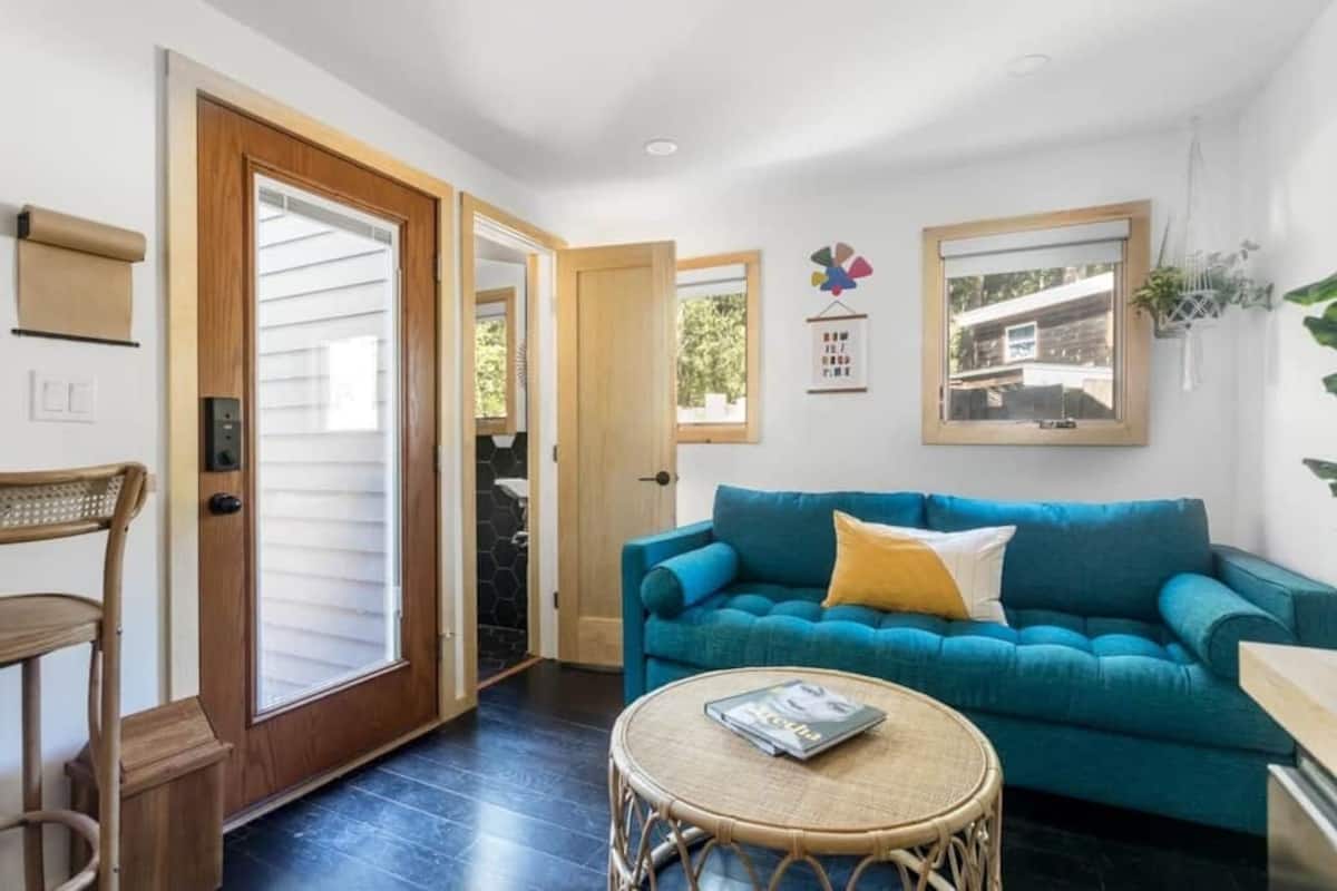 A living room with a teal sofa, a round wicker coffee table, and a door leading to a balcony.