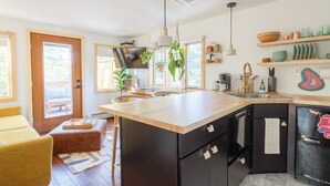 A modern kitchen with a wooden island, black cabinets, and a built-in refrigerator. There are hanging plants, a coffee machine, and shelves with dishes and utensils. - The Herwood Inn (Woodstock)