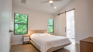 A bedroom with a bed, two windows, a ceiling fan, and a door leading to another room.
