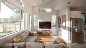 A modern living room with a large TV, a sofa, a coffee table, and a kitchen area with a refrigerator.