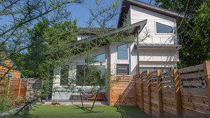 A modern two-story house with a wooden fence, a hammock, and a small garden area.