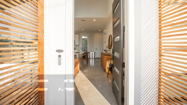 A hallway with wooden slats on the walls, leading to a kitchen area with a refrigerator and a dining table.