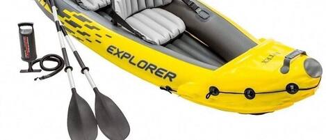 A yellow inflatable kayak with the word "EXPLORER" on it, two paddles, and a pump.