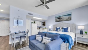 A modern bedroom with a bed, a blue sofa, a dining table, and a kitchen area.